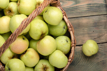 Ripe freshly picked apples in a basket on a wooden background.