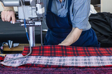Female worker on a sewing manufacture uses electric cutting fabric machine. Textile industry, clothing production, fabric cutting