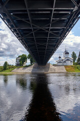 Bottom view of the chain bridge in the city of Ostrov, the old church, the stone embankment, the river