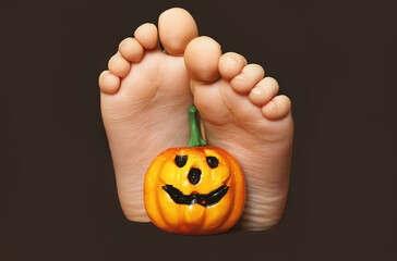 The legs of a little girl with a pumpkin lie on a dark background. Pumpkin Jack close-up, next to...