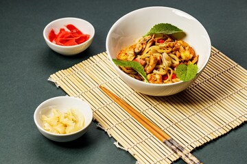 WOK noodles with seafood and vegetables. Mussels, shrimps and squids fried in oil. Delicious Asian lunch in a white bowl on a bamboo mat. Stir fry noodles. Traditional asian food. Still life.