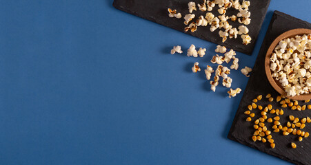 Popcorn on slate tray and corn seeds on blue background. Flat lay. Copy space. Home movie time.