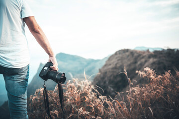 Male photographer holding DSLR camera ready to take landscape photos and mountain scenery, with blur mountain background, to people and nature concept.