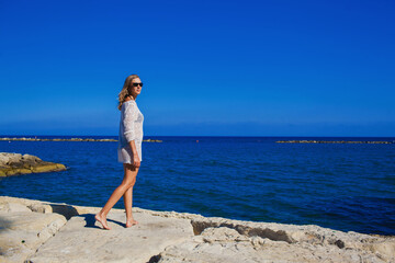 A beautiful girl stands on the rocky shore of the Mediterranean Sea Cyprus.Cheerful girl rests on the sea