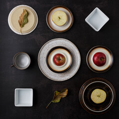 Flat lay creative concept of fallen autumn leaves and red apples on a plates and in cups. Dark background. Season concept.