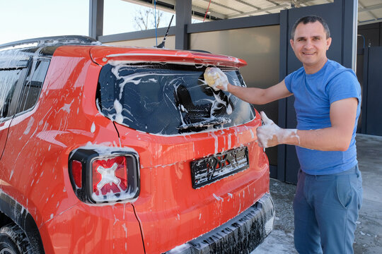 Happy man washes a car at a car wash. Car in foam