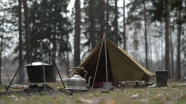 A close-up of teapot and mug at the camping against the backdrop of a tent.