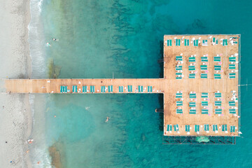 Top down aerial view of wooden pier with sunbeds and umbrellas. Mediterranean sea coast