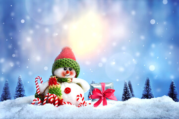 Cheerful snowman with gift box and candy cane on the snow. Christmas background.
