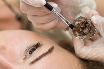 A young girl is undergoing a procedure for correcting and coloring her eyebrows. Master of cooking...