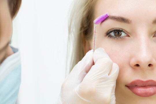 A young woman combs her eyebrows with a pink brush. Eyebrow correction, henna staining. Close-up. Half of the face.