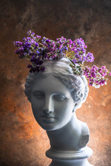 Plaster bust of the beautiful Aphrodite with flowers on her head on a rusty antique background.