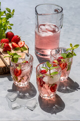Homemade lemonade with mint and strawberries in a jug and three glasses on a gray table. Cold red drink.