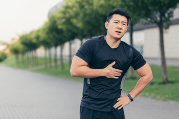 Male asian athlete, has chest pain fitness in the park and running, heart aches after cardio...