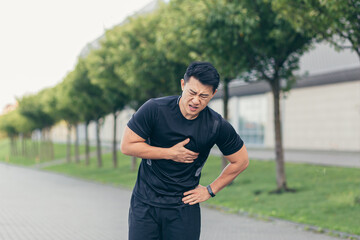 Male asian athlete, has chest pain fitness in the park and running, heart aches after cardio...