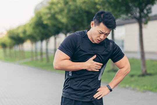 Male asian athlete, has chest pain fitness in the park and running, heart aches after cardio exercise