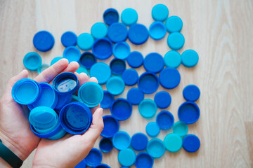Person Holding bottle caps. background of blue plastic bottle caps. Recycling concept. 