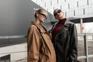 two beautiful fashionable girls with sunglasses in a stylish leather jacket posing on the street in the city