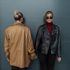 Two young girls model in fashionable clothes with a leather jacket and black jeans are standing near a metal wall outdoors. Front and back of a woman concept art