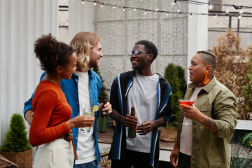 Waist up portrait of diverse group of young people having fun at outdoor rooftop party and chatting