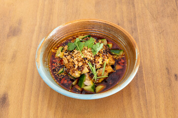 Spicy chicken ramen with pieces of zucchini, peanuts, parsley and sesame seeds in ceramic bowl