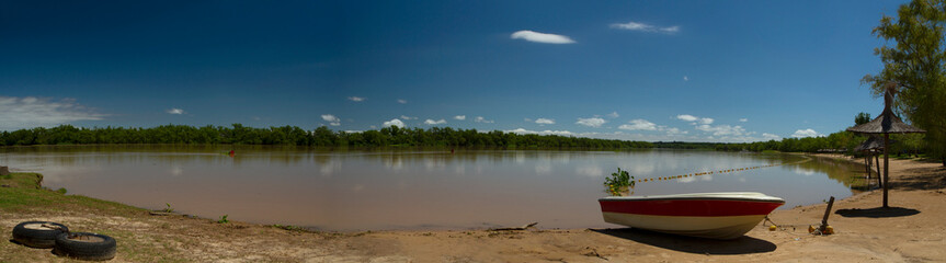 Panorama view of the river shore in a summer sunny day. A boat in the sand in the foreground and the tropical jungle in the background reflected in the water.  