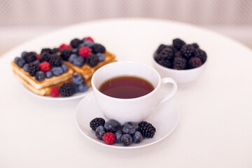 Morning breakfast with cup of tea, waffles and berries