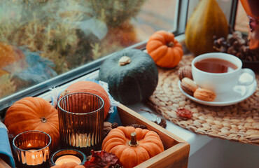 Autumn cozy composition. Pumpkins, candles, fall leaves on wooden tray and cup of hot tea with...