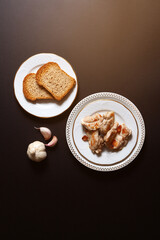 top view of grilled chicken plated with garlic and whole wheat bread on brown background