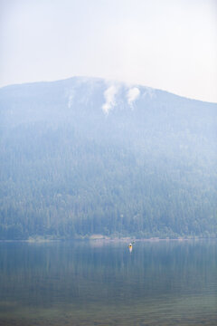 Wildfires burn on a forested mountain on July 16th, 2021, at Three Valley Gap lake, between Revelstoke and Sicamous, British-Columbia. The lake is cloaked in smoke from the fires raging in the area.
