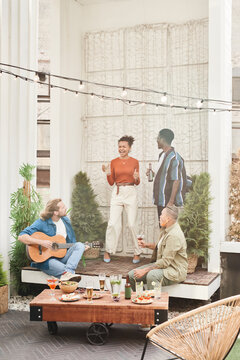 Vertical Full Length View At Diverse Group Of Friends Dancing During Outdoor Party At Rooftop, With Young Man Playing Guitar