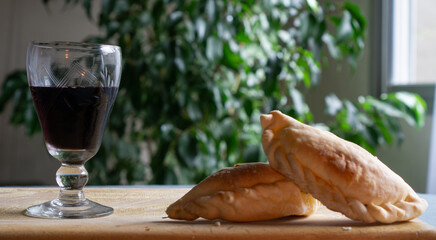 traditional Argentine food, an empanada or  patty on a wooden board and a glass of wine by its side