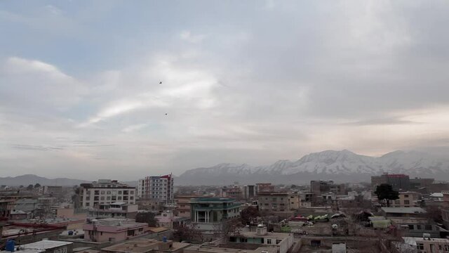 Afghanistan scene -wide angle shot of buildings with two fast moving helicopters passing over Kabul city - camera pans right and tilts up to the sky