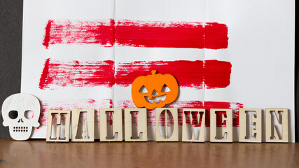 the word "halloween" in wooden stencil letters with a jack o lantern and a white skull with a red and white background