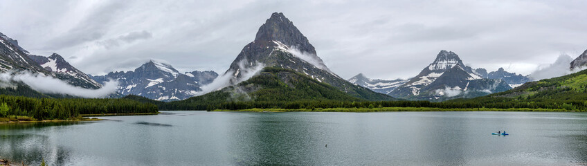 Swiftcurrent Lake - A kayak cruising on calm Swiftcurrent Lake, with rugged mountain peaks towering...