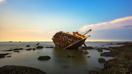 Boat deteriorate breaking down laying in the coast side with sunset in background