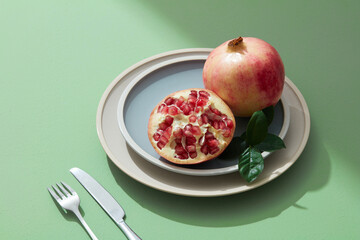 Still life of red pomegranate fruit, seed, half on pastel plate with light green background. 