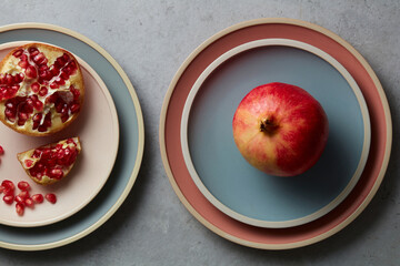 Fresh Pomegranates and sliced ​​pomegranate pieces on Ceramic pastel plate on grey concrete background decoration. Colorful plates stacked on. Topview