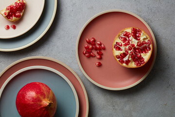 Fresh Pomegranates and sliced ​​pomegranate pieces on Ceramic pastel plate on grey concrete background decoration. Colorful plates stacked. Topview