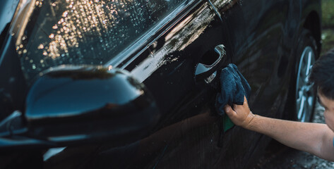 The guy wipes the front door of the car with rag