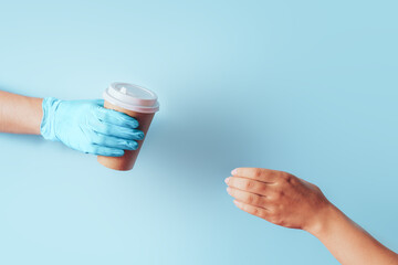 Hand in blue glove passes paper coffee cup to the other hand against blue background