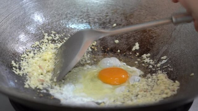 Crack the eggs on the fried galic in the pan with oil on gas stove.
