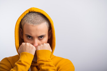 Young woman in ocher hood holding fists near face on white background.