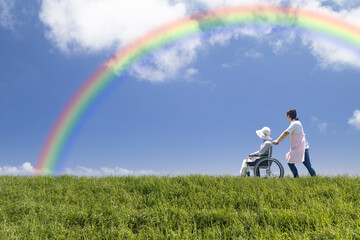 虹の下を散歩するヘルパーと高齢者
