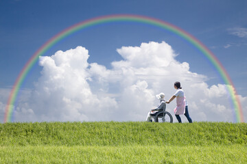 虹の下を散歩するヘルパーと高齢者