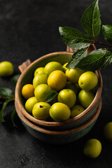 yellow freshly torn cherry plum with green leaves in ceramic cups on a gray background, close-up