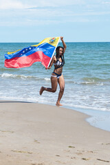 Happy woman holding a Venezuelan flag while running along the beach.