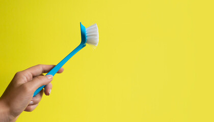 Female hand holding house cleaning scrubbing brush tool on yellow background.