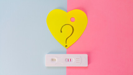 The hCG test lies on a blue and pink background and shows two red lines. A heart-shaped sticker...