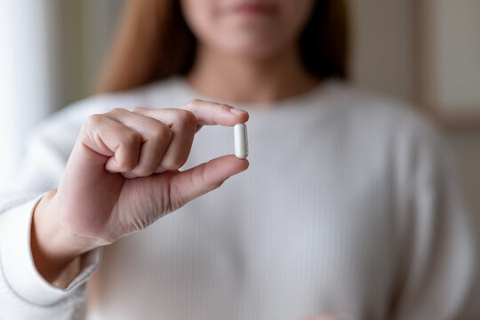 A woman holding and showing white medicine capsules in hand